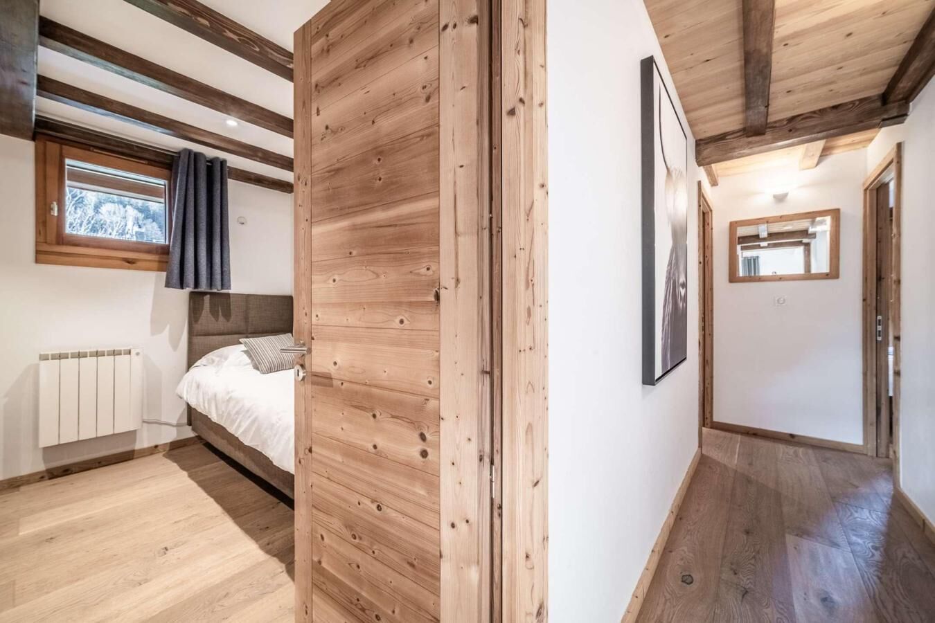 A bedroom with a wooden ceiling, a bed, a radiator, and a window with curtains.
