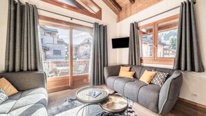 Een moderne woonkamer met een grijze bank, een ronde salontafel en een groot raam met gordijnen.