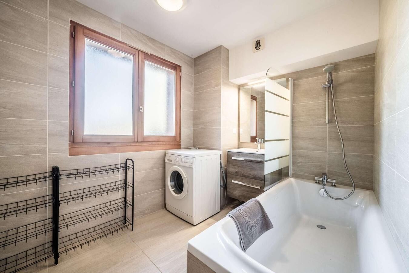 A modern bathroom with a built-in washing machine, a bathtub, and a shower.