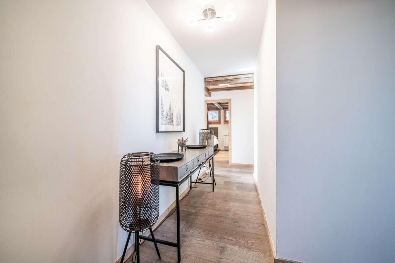 A hallway with a wooden floor, a metal chair, a table with a tray, and a framed picture on the wall.