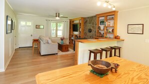 Amplia sala de estar con mesa de comedor de madera, cocina con salpicadero de piedra y zona de estar acogedora con sofá y mesita de centro.
