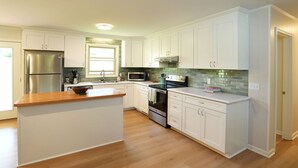 Una cocina moderna con armarios blancos, una isla central, electrodomésticos de acero inoxidable y encimera de madera.