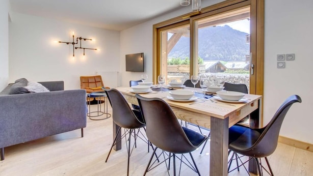 A modern dining area with a wooden table set for four, surrounded by black chairs. A grey sofa and a wooden chair are visible in the background. - 200m from ski slopes, Ground floor, terrace, tv, 42m², Morzine (Morzine)