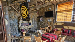 A rustic interior with a stone fireplace, wooden furniture, and a television mounted on the wall. - Petra dad farm (Shamakh)