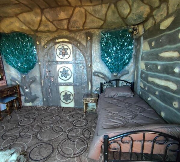 A room with a stone wall, a bed with a patterned headboard, a small table, and a decorative door with floral designs.