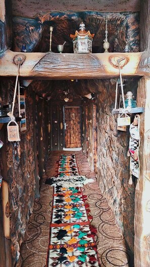 A narrow hallway with a patterned carpet, rustic walls, and hanging decorations.