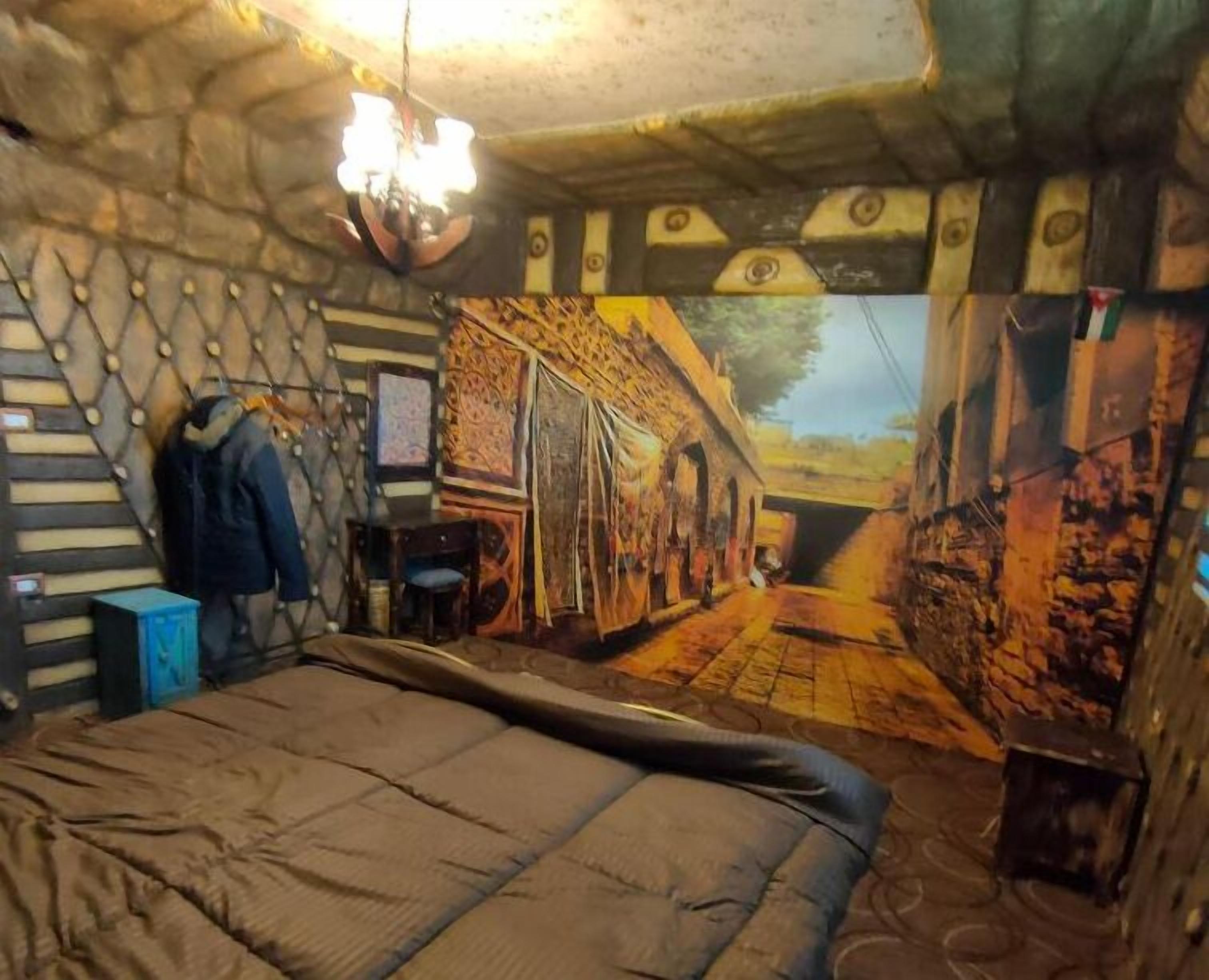 A room with a bed, a desk, and a chair. There is a window with a view of a street.