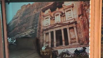 A room with a bed, a small table, and a wall mural of ancient ruins.