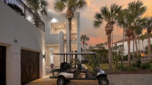 A golf cart parked in front of a building with a garage, palm trees, and a sunset sky. - Private Heated Pool - Golf Cart Included (Destin)
