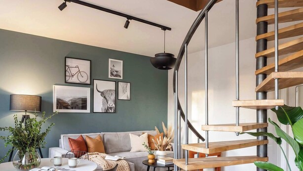 A modern living room with a wooden staircase, a dining area, and a sofa set.