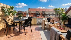 A rooftop terrace with a table and chairs, a sofa, and potted plants.