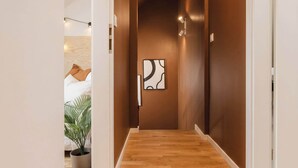 A hallway with wooden flooring, white walls, and a brown accent wall. There is a framed artwork on the brown wall and a potted plant on the left.