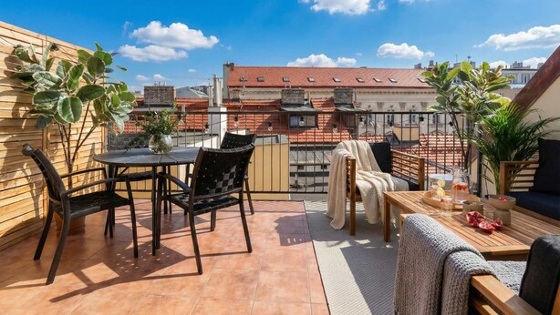 A rooftop terrace with a table and chairs, a sofa, and potted plants.
