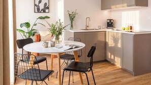 A modern kitchen with a dining area, featuring a round table, chairs, a coffee machine, and a plant.