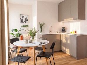 A modern kitchen with a dining area, featuring a round table, chairs, a coffee machine, and a plant.