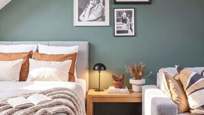 A bedroom with a sloped ceiling, a bed with white and brown bedding, a bedside table with a lamp, and framed pictures on the wall.