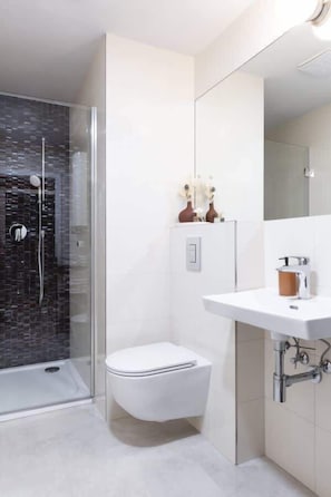 A modern bathroom with a glass-enclosed shower, a white toilet, and a white sink with a mirror above it.
