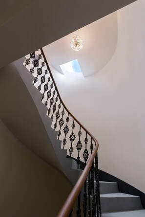 A curved staircase with ornate black railings and a modern light fixture at the top.