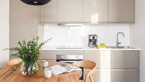 Une cuisine moderne avec des meubles blancs, une machine à café et un coin repas comprenant une table, des chaises et une plante.