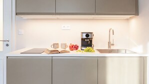 A modern kitchen with a built-in coffee machine, a sink, and a countertop with a book, two cups, and a pomegranate. - TurnKey | Republic Square Apartment I (Praha 1)