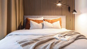 A neatly made bed with white and brown bedding, a knitted blanket, and a pair of glasses on an open book. - TurnKey | Republic Square Apartment I (Praha 1)