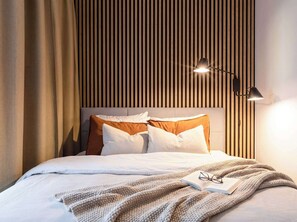 A neatly made bed with white and brown bedding, a knitted blanket, and a pair of glasses on an open book. - TurnKey | Republic Square Apartment I (Praha 1)