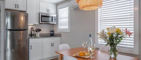 A modern kitchen with white cabinets, stainless steel appliances, and a wooden dining table set with a cheese platter and wine glasses.