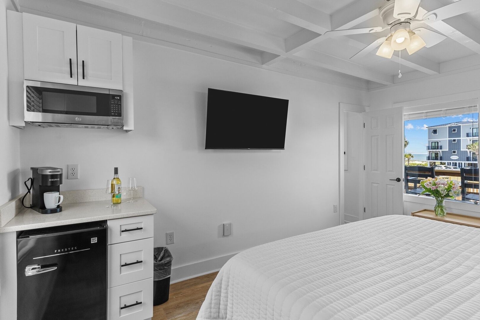 Un dormitorio moderno con una cama, un televisor de pantalla plana, una kitchenette con microondas, cafetera y un cesto de basura.