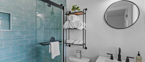 A modern bathroom with a glass shower enclosure, a toilet, a sink with a mirror, and a towel rack with neatly folded towels.
