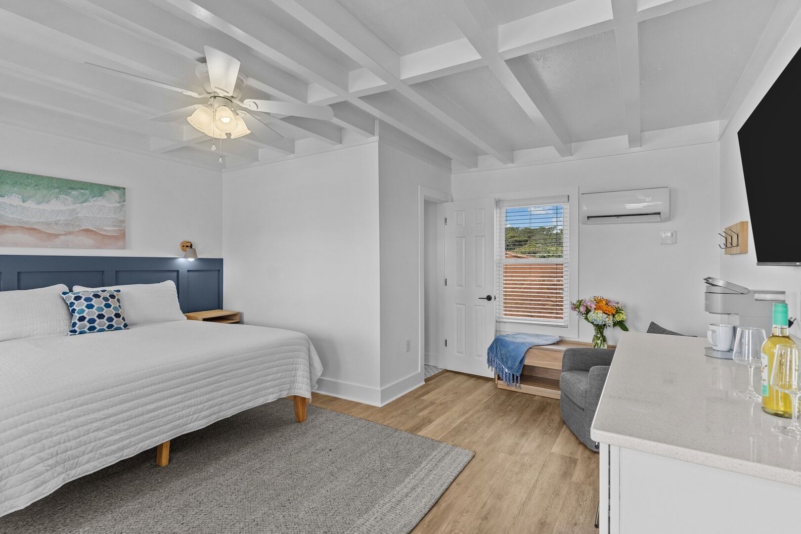 A bedroom with a bed, a nightstand, a desk, and a chair. There is a door leading to a balcony.