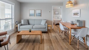 A modern living room with a grey sofa, a wooden coffee table, and a dining area with a wooden table and chairs.