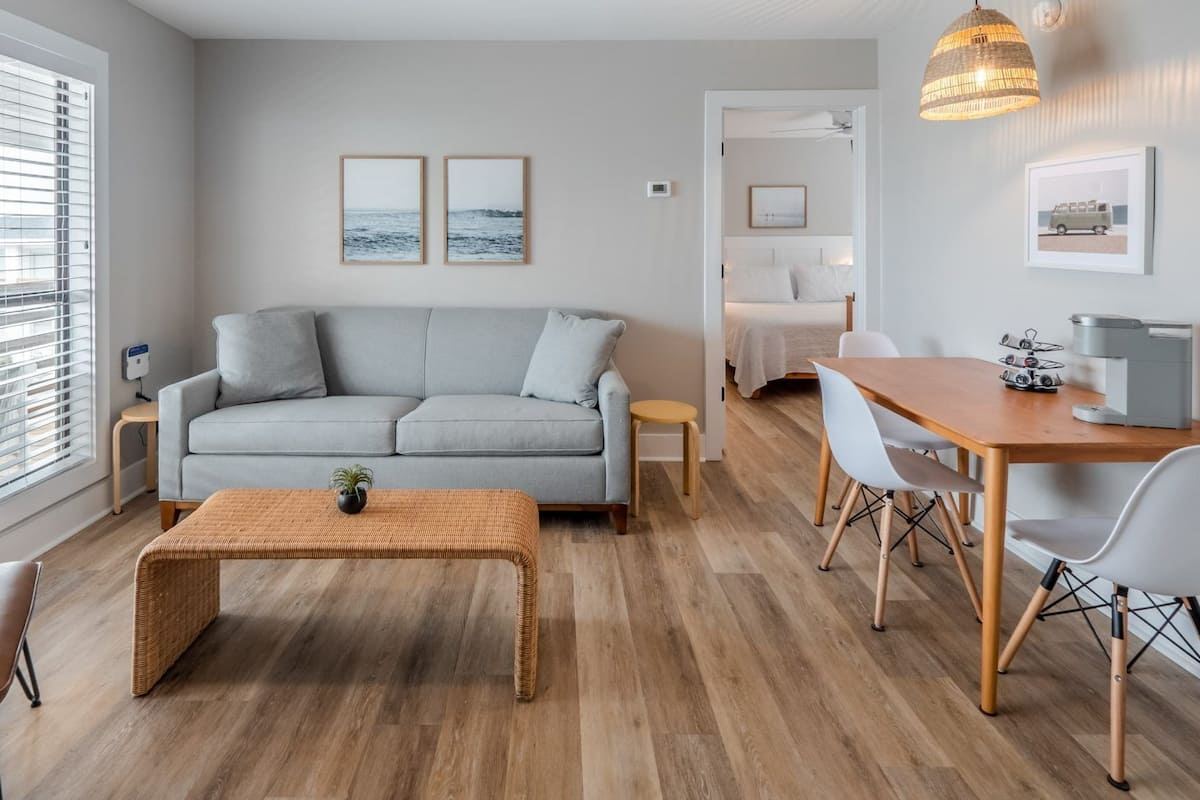A modern living room with a grey sofa, a wooden coffee table, and a dining area with a wooden table and chairs.