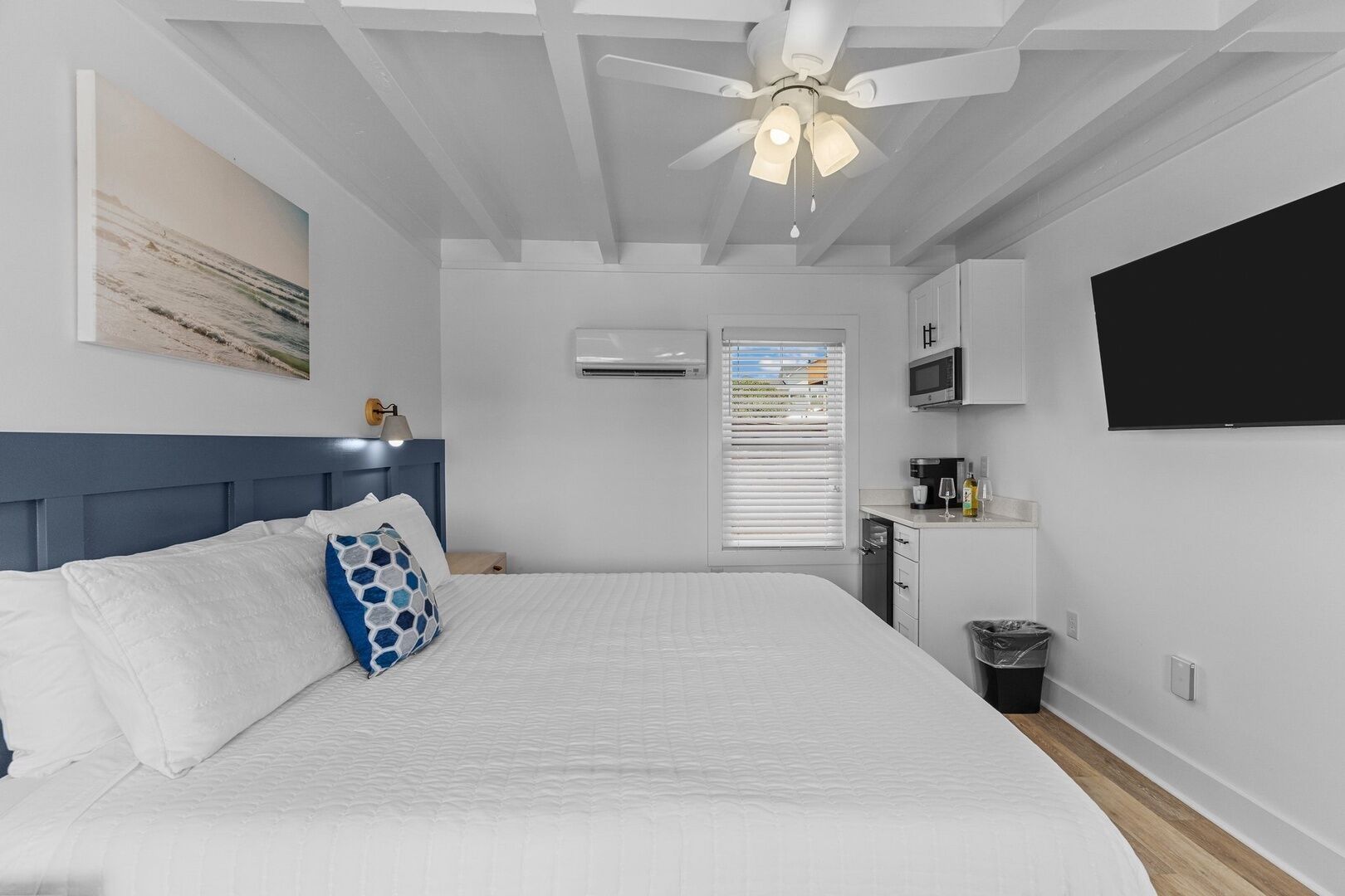 Una camera da letto con un letto grande, una ventola a soffitto, una TV a parete e un angolo cottura.