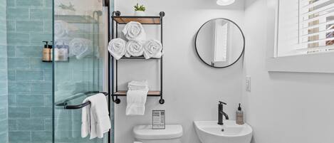 Un baño moderno con cabina de ducha de vidrio, inodoro, lavamanos y toallero con toallas dobladas con esmero.