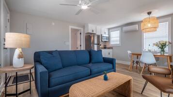 A modern living room with a blue sofa, a small side table with a lamp, a wicker coffee table, and a ceiling fan.