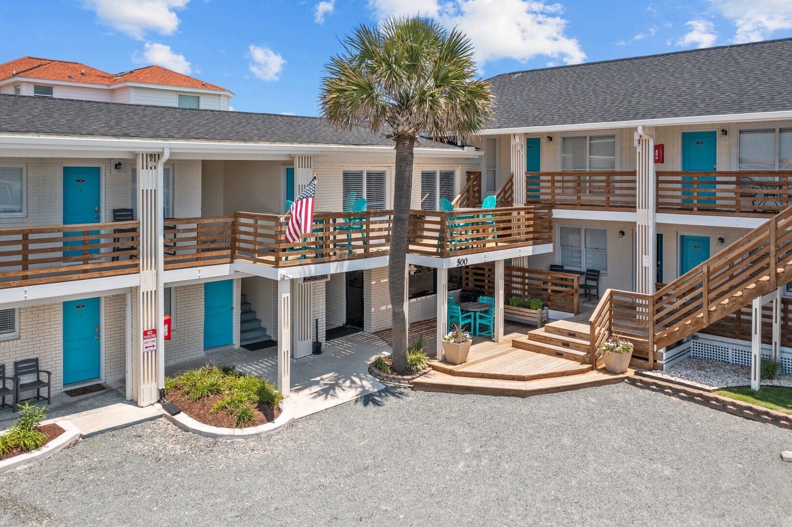 Un motel de varios pisos con un patio central, mobiliario exterior y una bandera.