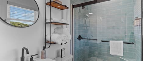 A modern bathroom with a glass shower enclosure, a sink with a mirror, and towel racks.
