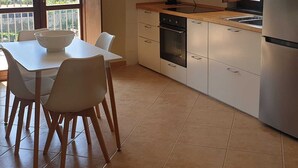 A modern kitchen with white cabinets, a built-in oven, and a stainless steel refrigerator. There is a dining table with chairs and a window overlooking a green landscape. - La Finestra sul mare Sorrento (Piano di Sorrento)