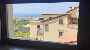 A window view of a building with a tiled roof and multiple windows, overlooking a coastal area with buildings and greenery. - La Finestra sul mare Sorrento (Piano di Sorrento)