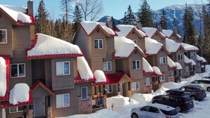 Una hilera de edificios de madera con techos rojos, cubiertos de nieve, y coches aparcados delante.