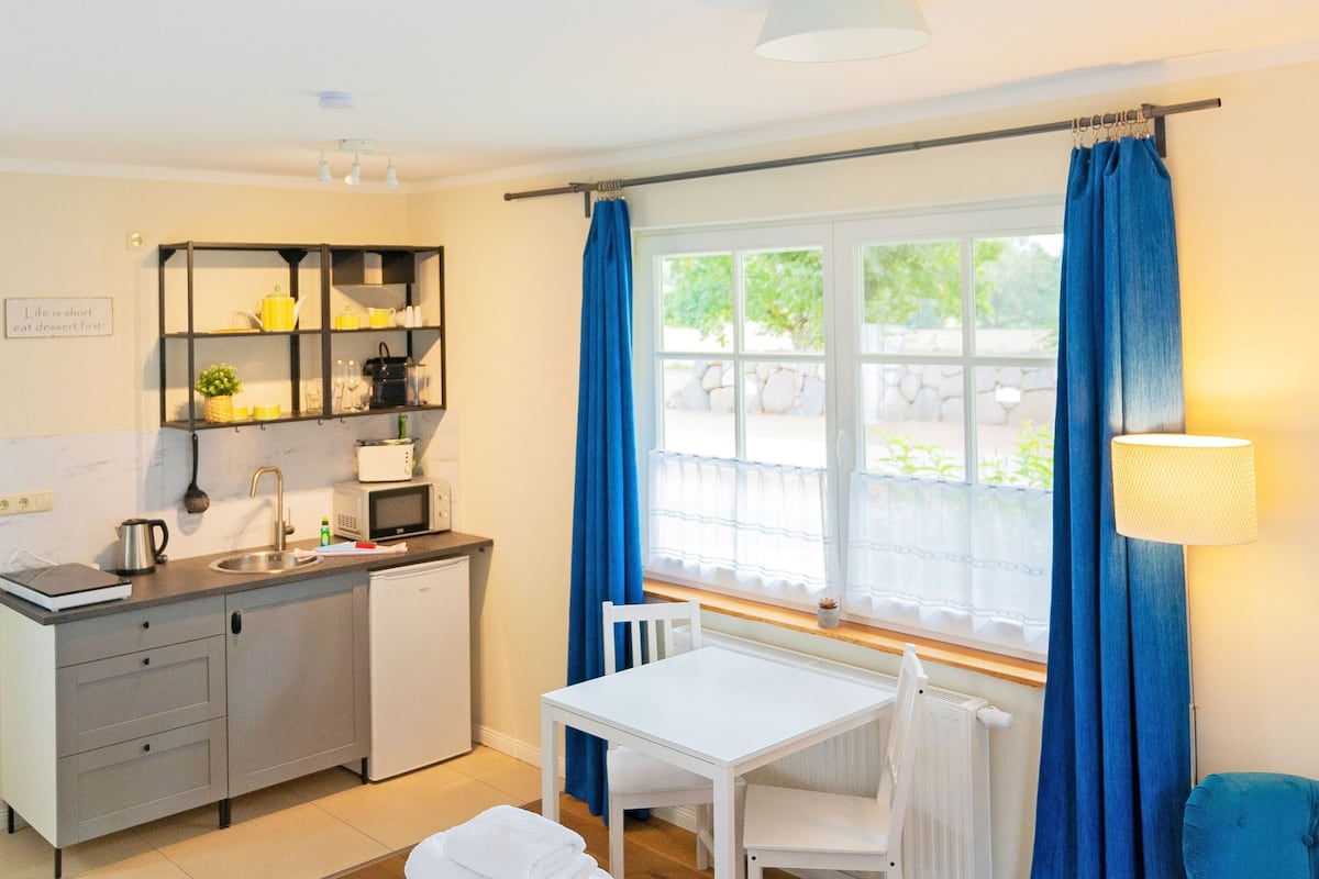 A compact kitchen with a dining area, a window with curtains, and a small table.