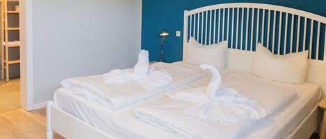 A neatly made bed with white linens and two towels shaped like swans, a bedside lamp, and a wooden nightstand.