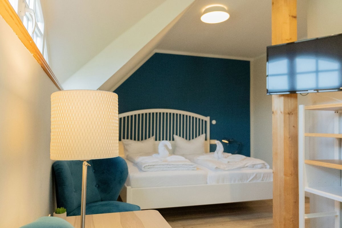 A bedroom with a bed, a bedside table, a lamp, a chair, and a TV.
