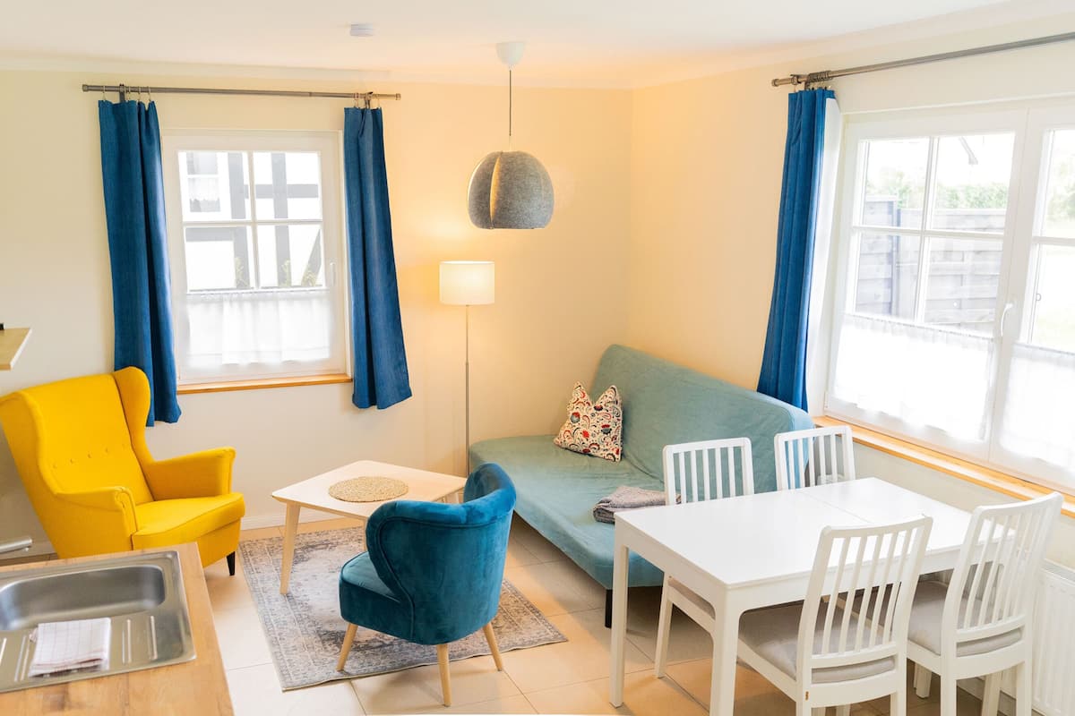 A compact living space with a sofa, a dining table with chairs, a small kitchen area with a sink, and a lamp.