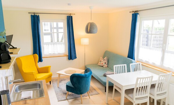 A compact living space with a sofa, a dining table with chairs, a small kitchen area with a sink, and a lamp.
