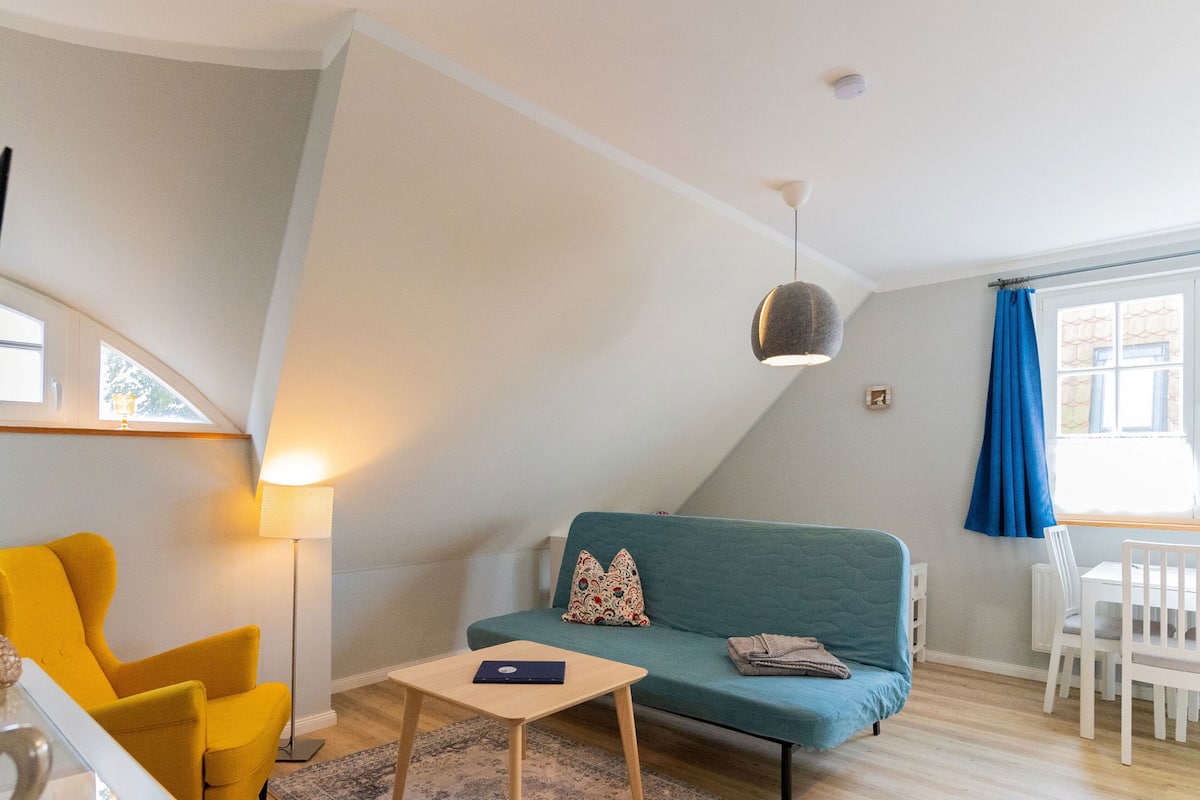 A cozy living room with a teal sofa, a yellow armchair, a small wooden table, and a floor lamp.