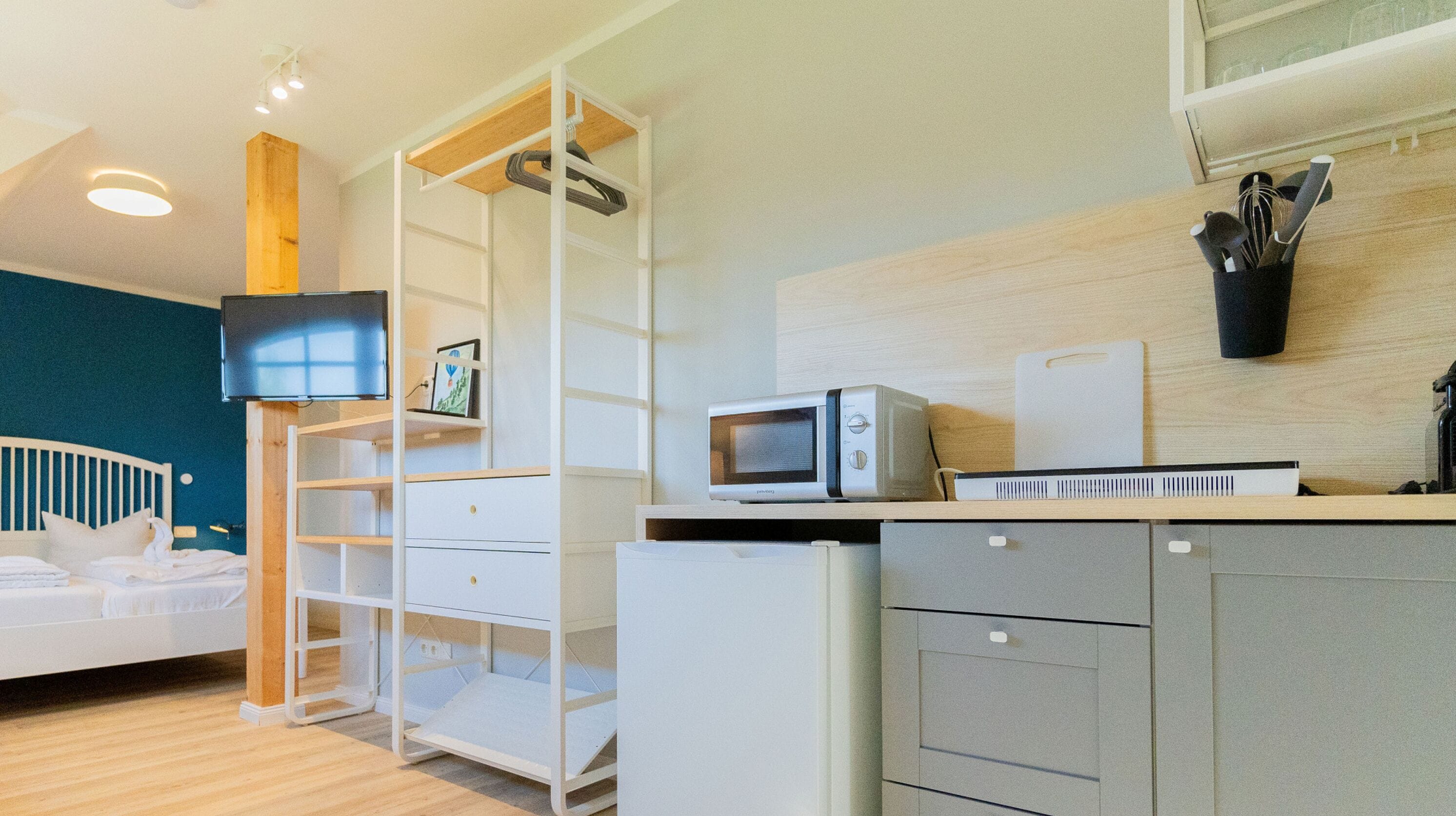 Una cocina moderna equipada con microondas, tostadora y cafetera. Hay una cama con ropa blanca y un televisor montado en la pared.