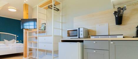 Una cocina moderna equipada con microondas, tostadora y cafetera. Hay una cama con ropa blanca y un televisor montado en la pared.