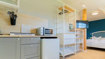 A modern hotel room with a kitchenette, a flat-screen TV, a bed, and a wooden ceiling.