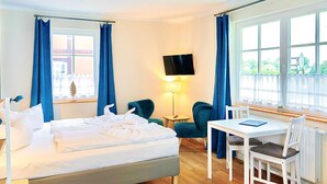 Ein Hotelzimmer mit Bett, Schreibtisch, zwei Stühlen, Fernseher und einem Fenster mit Vorhängen.